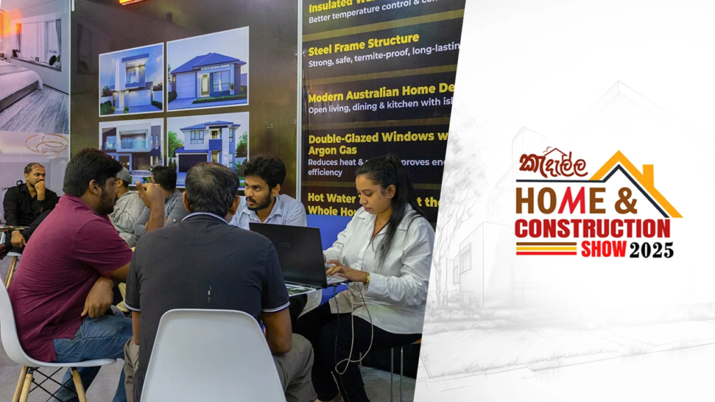 Group of people at a trade-show booth discussing with a presenter using a laptop, with house images on display behind them.